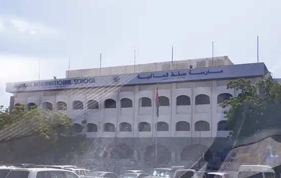 The main building of Muscat International School, featuring the main entrance view and several cars parked in front